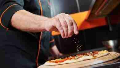 hand of chef baker in uniform adding spice into pizza after pizz